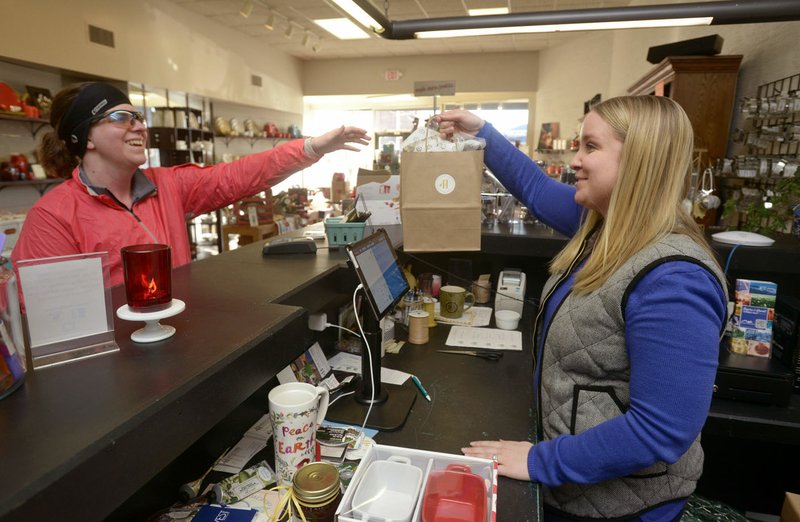 Melissa Turpin (right) sells a set of drinking glasses to Julie Wylie of Rogers Saturday at Honeycomb Kitchen Shop in downtown Rogers. Turpin and Dana Smith opened the business in April after renovating the space on West Walnut Street to include a kitchen where cooking classes will be offered.