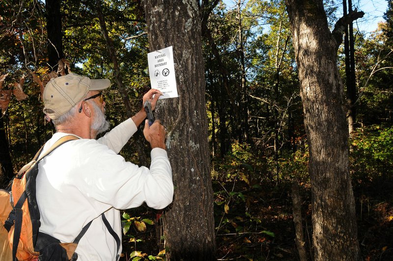 Steve Sampers with Northwest Arkansas Master Naturalists places boundardy signs Oct. 21 during a work day at Sweden Creek Falls Natural Area near Kingston.