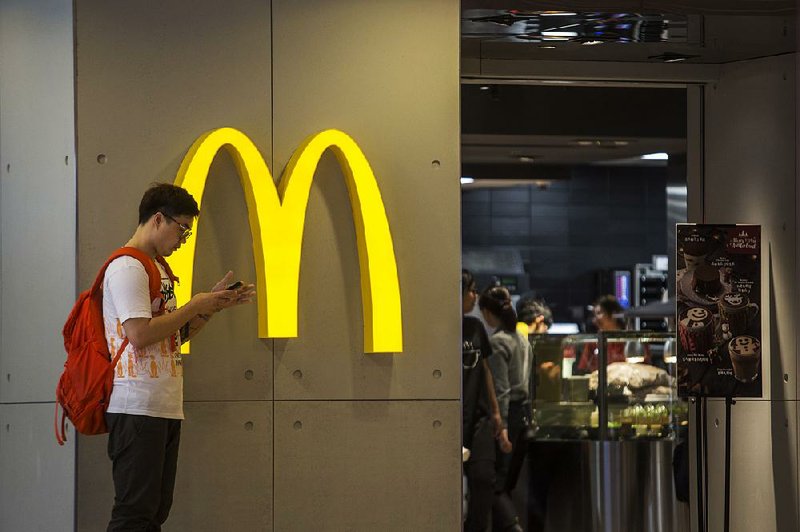 A man looks at his phone Monday outside a McDonald’s restaurant in Hong Kong. The burger chain has agreed to sell a controlling stake in its China and Hong Kong operations to a China-owned conglomerate and a private equity firm.
