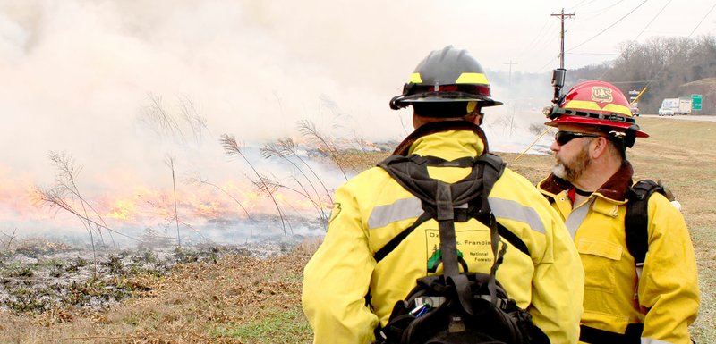 Keith Bryant/The Weekly Vista Arkansas Forestry Commission county ranger George Stowe-Rains, left, talks with ranger Scott VanHook while the overgrown wildflower meadow burns.