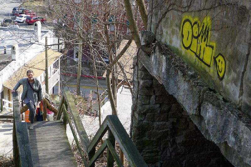 Margareta Rains of Ponca City, Okla., climbs the stairs to Center Street in Eureka Springs on Wednesday. Rains said she likes the bright yellow “D.I.M.” image on the wall, graffiti that has appeared in many spots around town.

