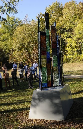 Dayton Castleman, third from right, talks about the trailside stained-glass sculpture, Ozarks Topopgraphy, S4R9T149, on Tuesday Oct. 21 2014 along the North Bentonville Trail. It is one of three sculptures celebrated by art enthusiasts and city officials during a walking tour along the trail Tuesday evening. The Bentonville Public Art Advisory Committee funded the three works. Others are SunKissed, which is a metal work of radiating spokes, and PAC-Man, a stone sculpture that depicts a person hiking. Ed Pennebaker of Osage, creator of Ozarks Topography, S4R9T149, is seen at foreground left.