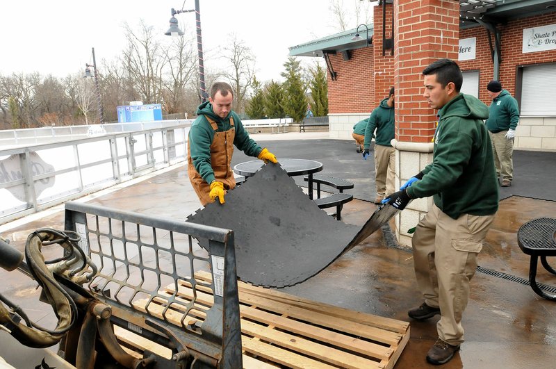 NWA Democrat-Gazette/FLIP PUTTHOFF John Francis (left) and Chris Flores with Bentonville Parks and Recreation remove padded flooring Wednesday at the Lawrence Plaza ice rink. Workers began thawing the ice and taking down the rink Wednesday.