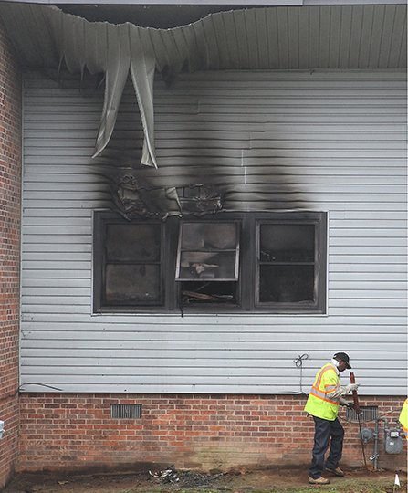 The Sentinel-Record/Richard Rasmussen AFTERMATH: An unidentified CenterPoint Energy gas company employee works around the gas meter near the burned-out back windows of Apt. 8 at 115 Wade St. on Thursday. Two local women died in the apartment following a fire in one of the bedrooms Wednesday night.