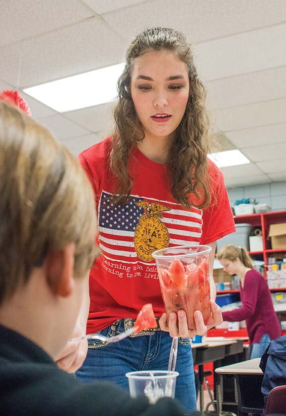 Students are served watermelon chunks by Glen Rose High School’s FFA president Grace Baker as she and fellow seniors show the kids how to make a parfait during a service project in which she and fellow seniors are teaching the younger students about agriculture.