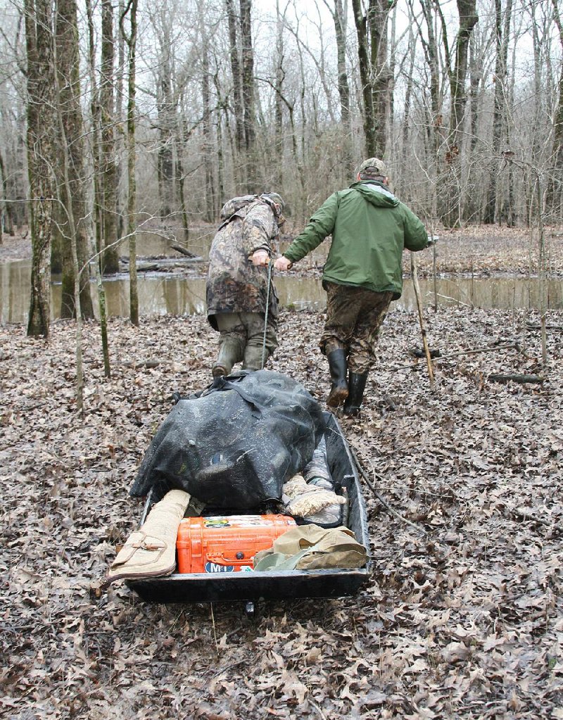 Jim Rose (left) and Connie Meskimen pull a homemade pirogue full of gear across dry ground after a hunt Tuesday in the Government Cypress Walk-in Area at Bayou Meto Wildlife Management Area.