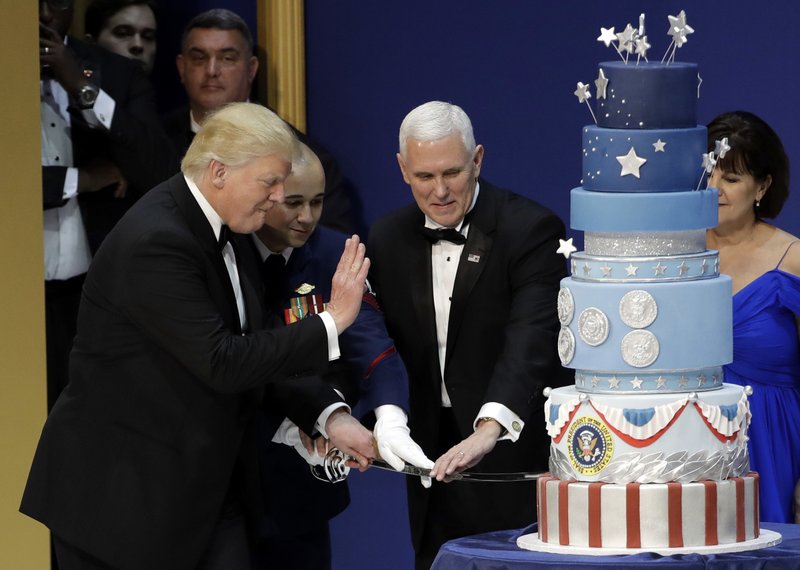 President Donald J. Trump, left, and Vice President Mike Pence, right, are helped by Coast Guard Petty Officer 2nd Class Matthew Babot, center, as they cut a cake at The Salute To Our Armed Services Inaugural Ball Friday, Jan. 20, 2017, in Washington. 