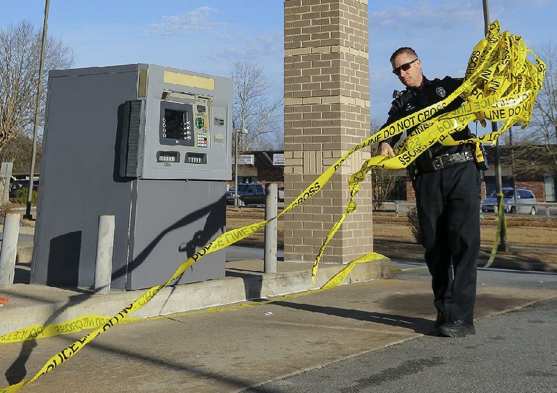 A Little Rock police officer removes crime-scene tape at Bank of the Ozarks on Otter Creek Parkway after detectives finished investigating a botched holdup that ended with one of the robbers being fatally shot.