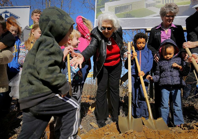 Amy Sanders reaches out to help a toddler climb a hill of dirt Wednesday during the groundbreaking ceremony for the new Amy Sanders Library along Johnson Drive in Sherwood. After the adults scooped a little ceremonial dirt, the children who frequent the library’s children’s programs were also invited to dig.  