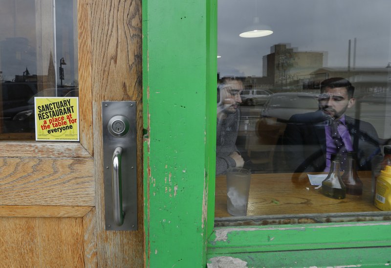In this Wednesday, Jan. 18, 2017 photo, a sanctuary restaurant sign is shown on the door of the Russell Street Deli in Detroit. Dozens of restaurants are seeking "sanctuary" status, a designation owners hope will help protect employees in an immigrant-heavy industry and tone down fiery rhetoric sparked by the presidential campaign.