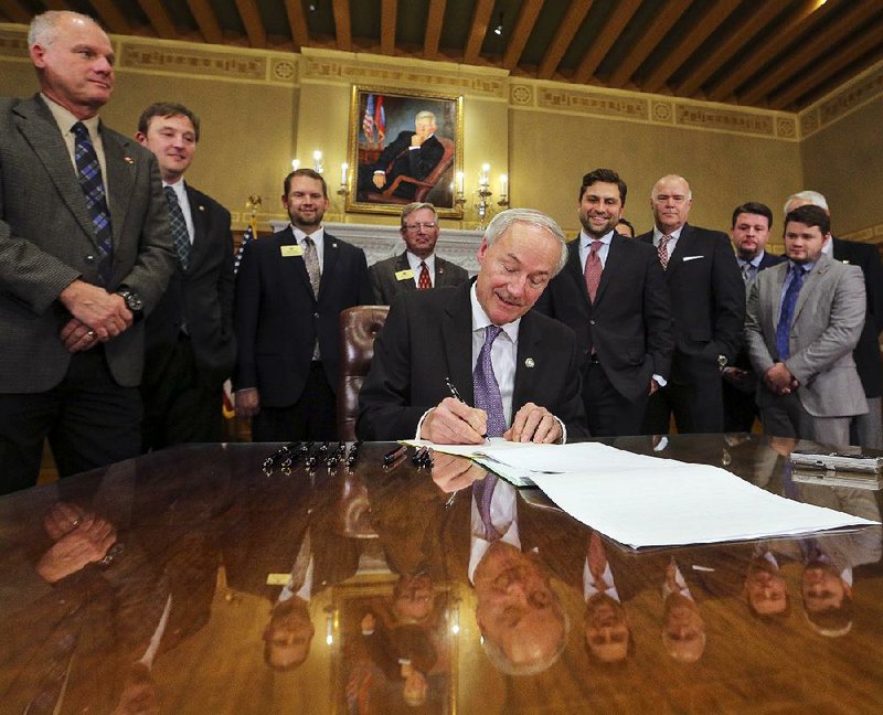 Surrounded by lawmakers Wednesday at the state Capitol, Gov. Asa Hutchinson signs legislation setting income-tax cuts for Arkansans who earn less than $21,000 in taxable income.