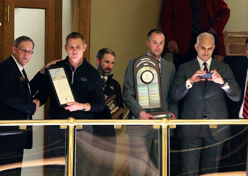 Arkansas State football Coach Blake Anderson (second from left) and other members of the athletic department display a plaque and show off Sun Belt Conference and Cure Bowl trophies for members of the House of Representatives at the State Capitol on Thursday. Anderson unveiled a signing class of 27 players Wednesday, including 14 junior college signees and two transfers from FBS schools. 