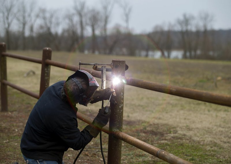 Walter Soucie with Siloam Springs’ Maintenance Department repairs a metal fence Thursday at the City Lake Park. The city will be breaking ground for park improvements Monday. “We are really going to get together and celebrate the fact that we have some amazing improvements coming and that we’re partnering with Ozark Off Road Cyclists,” said Holland Hayden, Siloam Springs communications director. 
