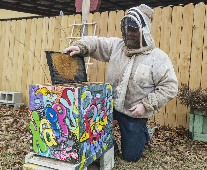 Wearing a protective jacket, Patrick Edwards shows a frame in a beehive outside his store, Preppers Bee Supply, on Thursday in Garfi eld. This hive will be filled with bees in the spring and will be put on the grounds at Crystal Bridges museum in Bentonville.