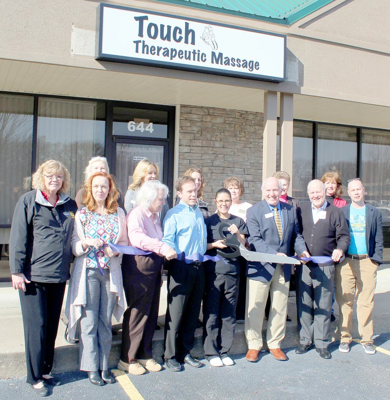 Keith Bryant/The Weekly Vista For Roeder, center, with scissors, cuts the ribbon at the grand opening for her business, Touch Therapeutic Massage, surrounded by members of the Bella Vista Business Association as well as her husband, Tom Roeder and Mayor Peter Christie.