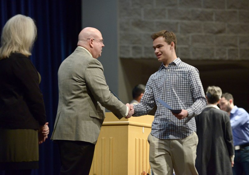 Dylan Moore, a sophomore at Rogers Heritage High, shakes hands with Lance Arbuckle, principal of Rogers New Technology High School, as he walks across the stage to receive his certificate of enrollment Sunday during an induction ceremony for the inaugural class of the Rogers Honors Academy at Rogers High School.