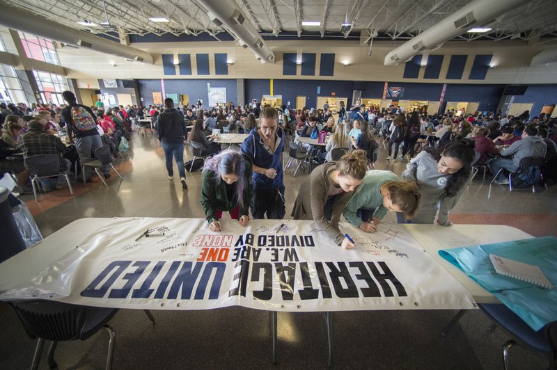 Students sign a banner Monday at Heritage High School in Rogers. The banner reads: “Heritage United: We are one, divided by none.” Students were encouraged to sign their name and add a message on what unites them as opposed to what divides them.