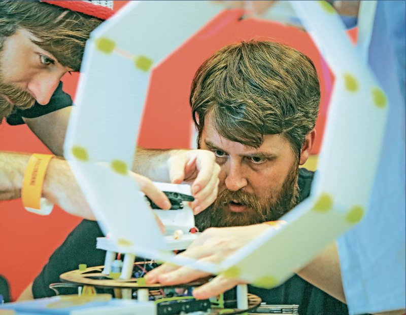 Teammates Shawn Goicoechea, left, and Ross Carroll work together on finishing touches as another teammate prepares an octagonal protector piece for their robot Saturday during the 2016 Beer, Brats & Bots event at the Arkansas Innovation Hub in North Little Rock. 