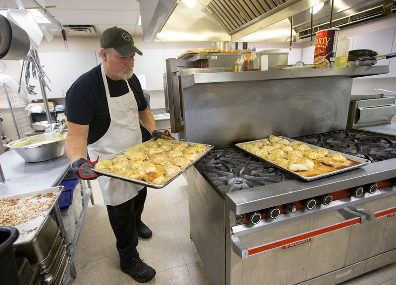 Doug Woods pulls a tray of chicken in January from the oven at the Benton County Senior Activity and Wellness Center in Bentonville. Woods, who has been the chef at the center for more than six months, prepares lunch daily for the Meals on Wheels program. The Northwest Arkansas Board of Realtors will host to the inaugural “League of Champions Luncheon” at 11:30 a.m. March 14 to benefit the nonprofit organization. 
