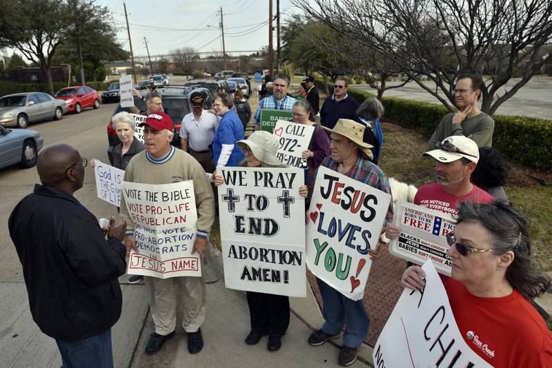 Dallas Police Sgt. Hall, left, speaks with Rives Grogan, 51, of Mansfield, Texas who wears a red Trump cap, and other anti-abortion protestors, informing them which sidewalks they can use to conduct their protest, outside of the Planned Parenthood South Dallas Surgical Health Services Center, Saturday morning, Feb. 11, 2017, in Dallas.