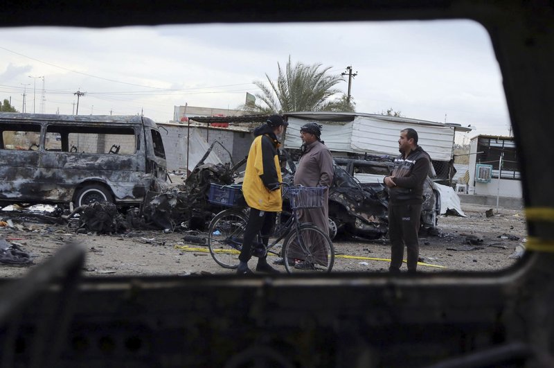 Civilians are seen through a broken window of a burned car at a used car dealer's parking lot in the southwestern al-Bayaa neighborhood, Baghdad, Iraq, Friday, Feb. 17, 2017, a day after a car bomb. The car bomb claimed by the Islamic State group killed scores of people. 