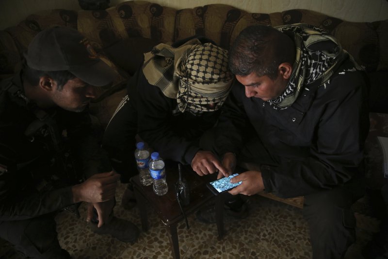 In this Nov. 25, 2016 photo, Special forces Lt. Col. Ali Hussein, right, listens to an Iraqi informant, center, giving information about Islamic State militant positions on a mobile map, in the Bakr front line neighborhood, in Mosul, Iraq. 