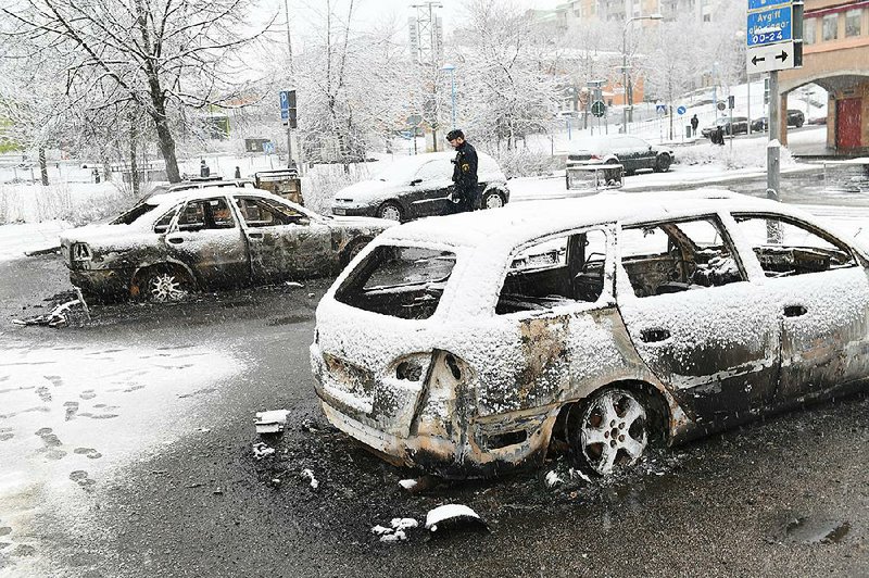 A Swedish policeman examines burned-out cars Tuesday in the Stockholm suburb of Rinkeby, where violence broke out.