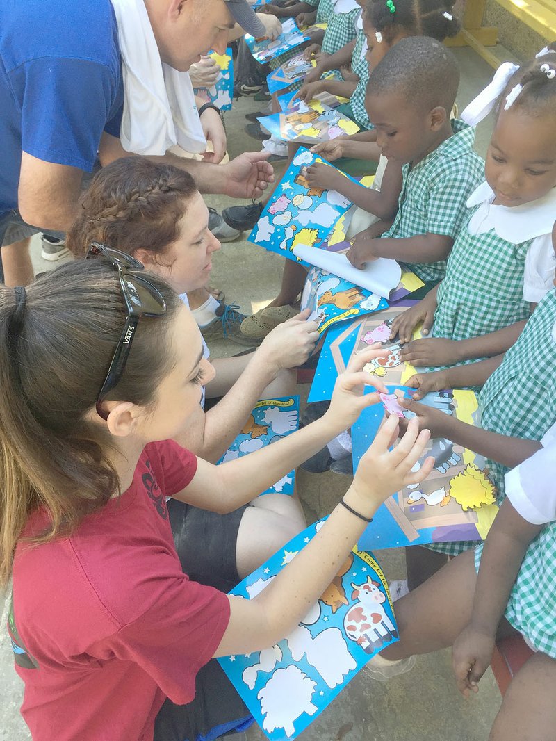 COURTESY PHOTO A group from Prairie Grove Christian Church help children in Haiti put stickers on an activitty page. The children attend a school in Haiti sponsored by Hope for Haiti, a non-profit organization.