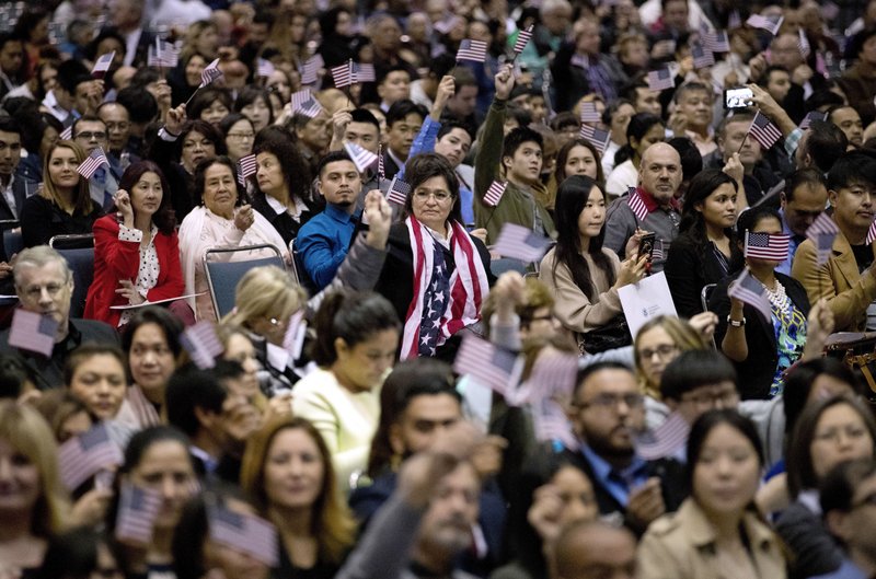 In this Wednesday, Feb. 15, 2017, file photo, people wave U.S. flags during a naturalization ceremony at the Los Angeles Convention Center, in Los Angeles. 