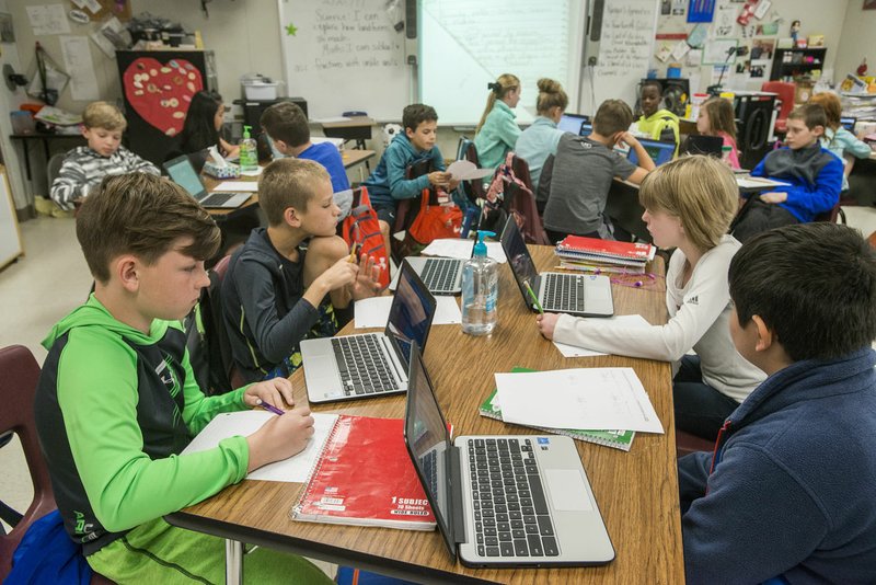 Fifth-graders Palmer Jurgensmeyer (from left), 11, Tuff Schureman, 10, Lily Still, 10, and Jai Gandhi, 11, finish their math assignment Thursday at Bellview Elementary School in Rogers. Bellview has received a lot of overflow students from other elementary schools filled to capacity.