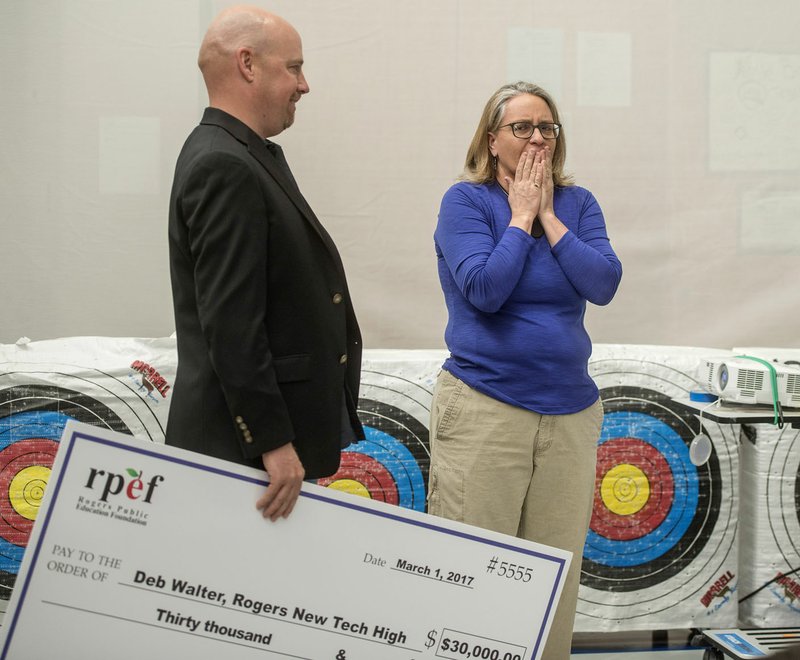 Deb Walter, a physical education teacher at New Tech High School, reacts Wednesday as Gaven Smith, vice president for the Rogers Public Education Foundation, tells her she will receive a $30,000 grant at the Rogers school. The grant will pay for a 16-foot climbing wall, mountain bikes and land paddles and outdoor education equipment. The grant is the second-funded by a special bequeathment of outdoors enthusiast George Merwin to the Rogers Public Education Foundation. Merwin died in 2014.