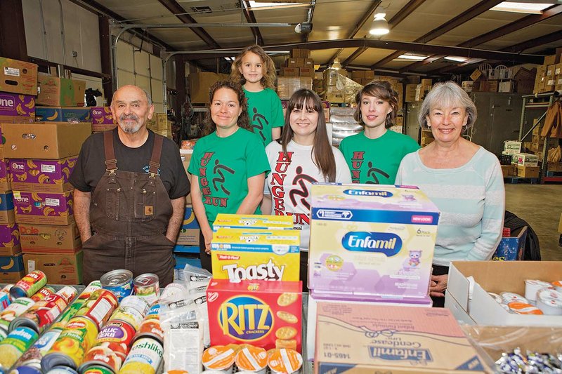 Claude Ruiz, from left, Meagin Warren, and Warren’s daughter, Cadence, back, Amy Acton, Jessica Crabtree and Karen Ruiz stand in the Choctaw Food Bank, one of the recipients of proceeds from the Clinton Hunger Run. The fifth-annual 5K run/walk is set for March 25. The Ruizes are co-directors of the food bank.
