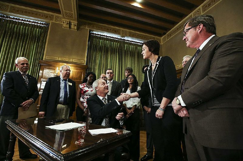 Gov. Asa Hutchinson (center) on Thursday congratulates Rep. Jana Della Rosa, R-Rogers, after signing a bill that provides financial help to students pursuing high-demand degrees at public twoyear colleges or technical schools. Della Rosa sponsored the bill.