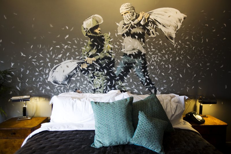 A Banksy wall painting showing Israeli border policeman and Palestinian in a pillow fight is seen in one of the rooms of the "The Walled Off Hotel" in the West Bank city of Bethlehem, Friday, March 3, 2017. The owner of a guest house packed with the elusive artist Banksy's work has opened the doors of his West Bank establishments to media, showcasing its unique "worst view in the world." The nine-room hotel named "The Walled Off Hotel" will officially open on March 11. (AP Photo/Dusan Vranic)
