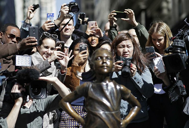 The statue Fearless Girl draws a crowd Wednesday as it appears to face down the famous charging bull sculpture on Wall Street in New York. The gathering was part of events around the world for the United Nations-designated International Women’s Day and for The Day Without Women protest in the United States, for which many women skipped work, joined marches or wore red to demonstrate the importance of women to the economy. 