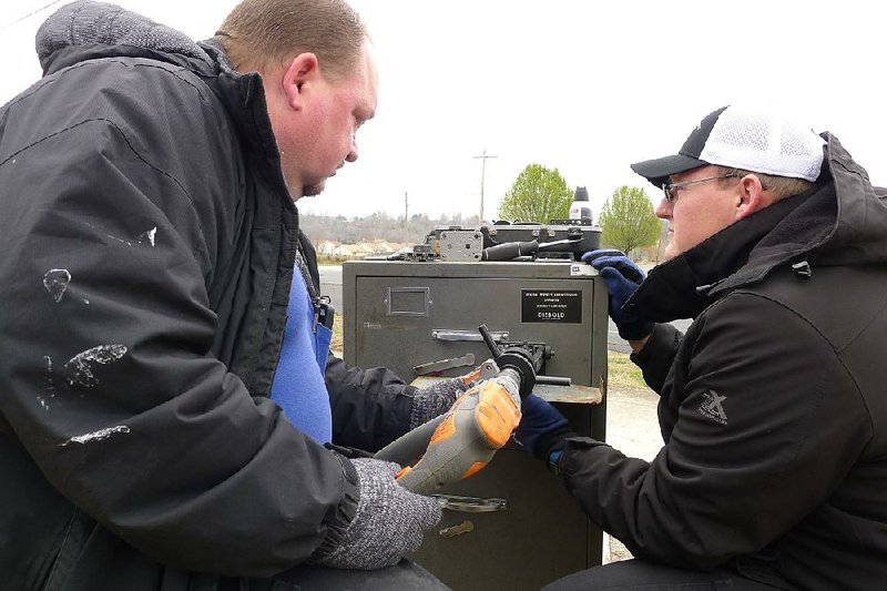 John Villines (left) drills a hole in a 52-year-old safe outside his shop in Harrison as his employee and brother-in-law Chris Black holds a tray under the drilling.