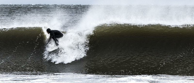 Surfer Billy Smith of Seaside Park, N.J., braves the 40-degree water temperature to ride a storm-churned wave at Seaside Heights, N.J., on Wednesday. The pounding waves caused erosion on some beaches in the Northeast.