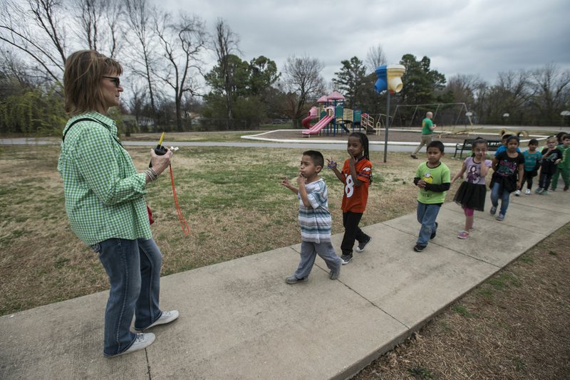 Mary Ann Brinkman leads her first-graders inside Friday after recess at Lee Elementary School in Springdale. Fencing around playgrounds varies among Northwest Arkansas schools. Some are enclosed while others are open.