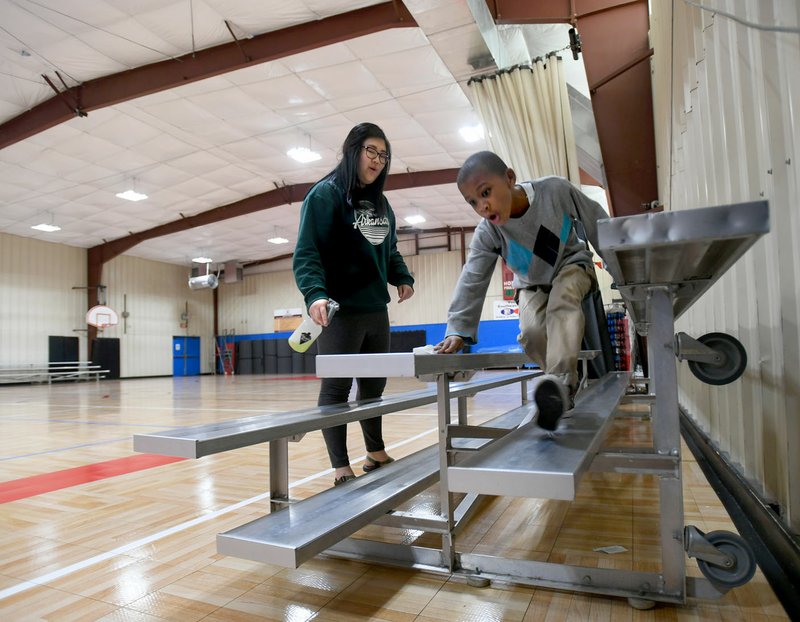 Ellis Stevenson (right), 6, helps volunteer Cindy Mao Friday as they clean the bleachers in the Yvonne Richardson Community Center in Fayetteville. City staff completed a lighting and insulation upgrade for the center in 2015 that included LED lighting inside the gymnasium as well as an LED lighting upgrade in gym that replaced 400-watt lights with brighter and more efficient 100-watt lights. The project was figured to have a 6-year pay back term. story.lead_photo.caption