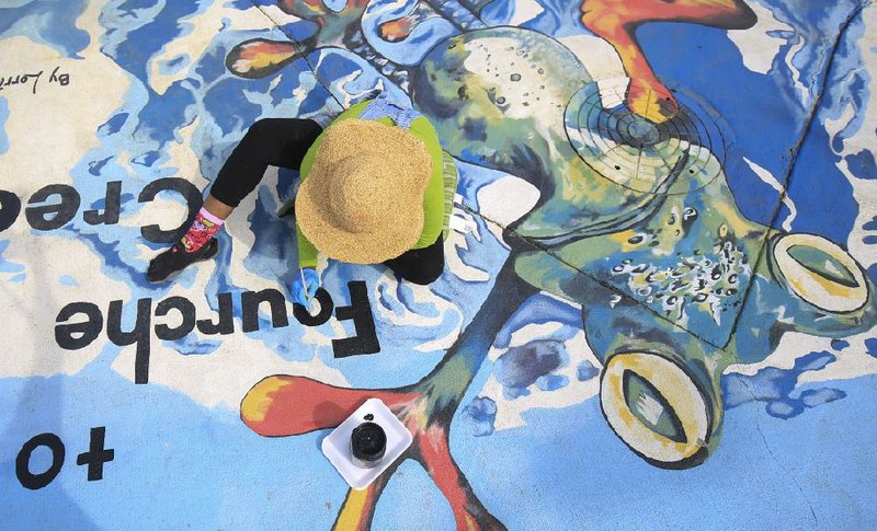 FILE — In this March 21, 2017 file photo, Lorria Grant-Eubanks at the corner of Markham Street and Fair Park Blvd. touching up the mural she painted in 2015 as part of the Drain Smart program. =