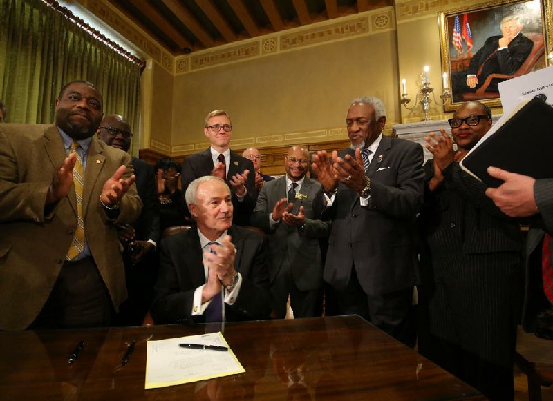 Surrounded by legislators, Gov. Asa Hutchinson lays down his pen Tuesday after signing the bill to separate the holidays recognizing civil-rights leader Martin Luther King Jr. and Confederate Gen. Robert E. Lee. With Hutchinson are (clockwise from left): Reps. Reginald Murdock, Fred Allen and Grant Hodges; Arkansas NAACP President Rizelle Aaron; and Reps. George McGill and Vivian Flowers.