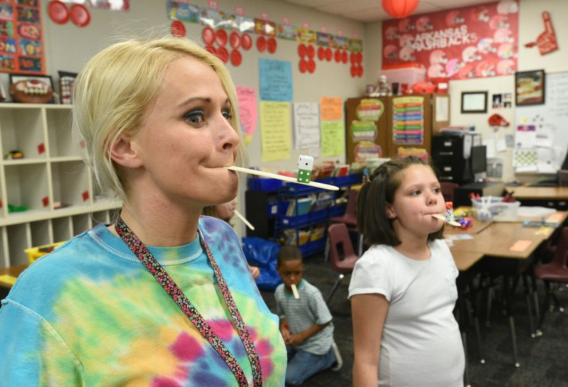Shannon Brown, a teacher at Adventure Club spring break camp, plays a game with students Tuesday to see how many dice they can balance on a stick. Students play games, do art and learn computer skills during the camp at Elm Tree Elementary School in Bentonville.