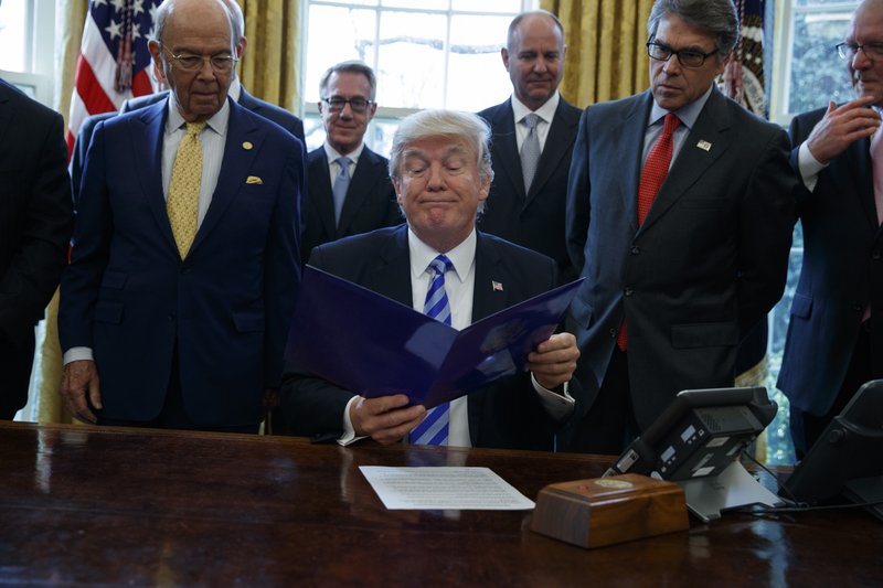 President Donald Trump, flanked by Commerce Secretary Wilbur Ross, left, and Energy Secretary Rick Perry, is seen in the Oval Office of the White House in Washington, Friday, March 24, 2107, where he announced the approval of a permit to build the Keystone XL pipeline, clearing the way for the $8 billion project. 