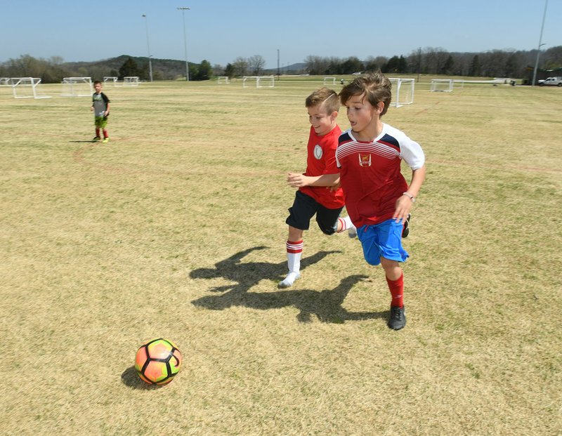 Mitch Kirkland (from right), 7, pushes the ball past Jackson Reno, 8, on Thursday as Jack Keathley, 8, watches during F.C. Arkansas practice at the Kessler Mountain Preserve and Regional Park in Fayetteville.