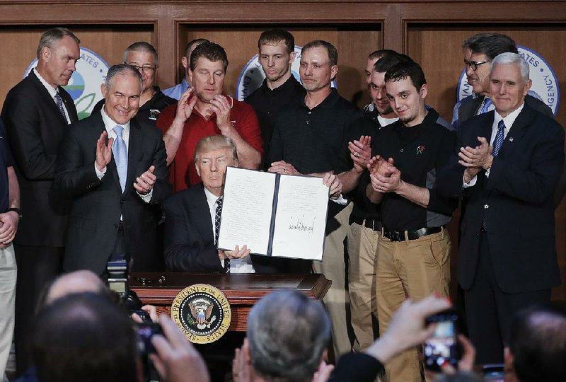 President Donald Trump, surrounded by coal miners, Interior Secretary Ryan Zinke, Environmental Protection Agency Director Scott Pruitt, Energy Secretary Rick Perry and Vice President Mike Pence, shows the executive order he signed Tuesday at EPA headquarters to roll back most of President Barack Obama’s climate and environmental policies. “We’re ending the theft of American prosperity and reviving our beloved economy,” Trump said. 