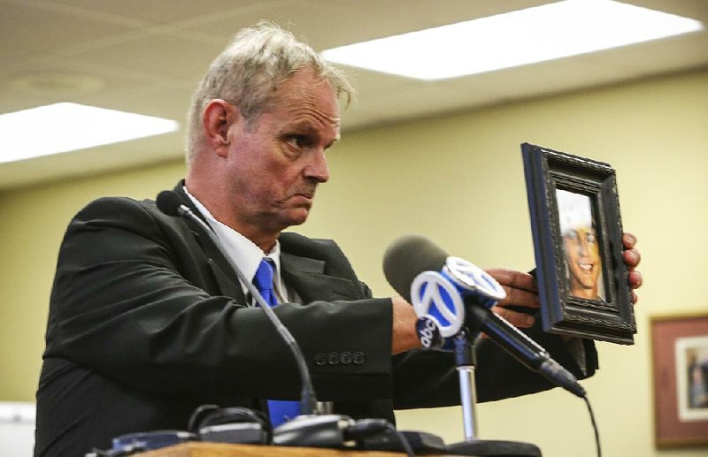 John Melbourne Sr. holds up a photo of his slain son, John Melbourne Jr., as he steps to the lectern during a Parole Board clemency hearing Friday in Little Rock.