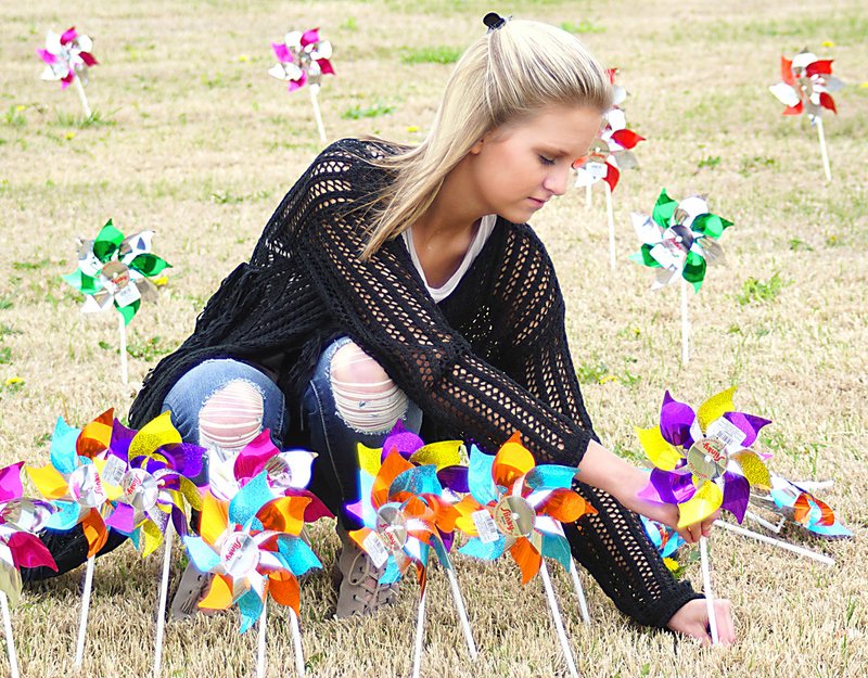 Photo by Randy Moll Kylie Bennett, a Gentry sophomore, places pinwheels on the lawn at Gentry Police Station on Friday. A total of 439 pinwheels were placed by the Gentry High School student council and police, representing the 439 cases of confirmed child abuse in Benton County. The pinwheels, to be on display during the month of April, are to raise awareness of the abuse and to encourage people to report it.