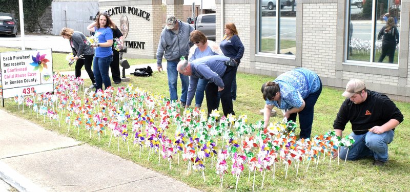 Photo by Mike Eckels A group of Decatur city officials, business leaders and residents plant 439 pinwheels March 31 in front of the Decatur police station on Main St. in Decatur. The pinwheels were planted as a reminder of the 439 confirmed child abuse cases in Benton County.