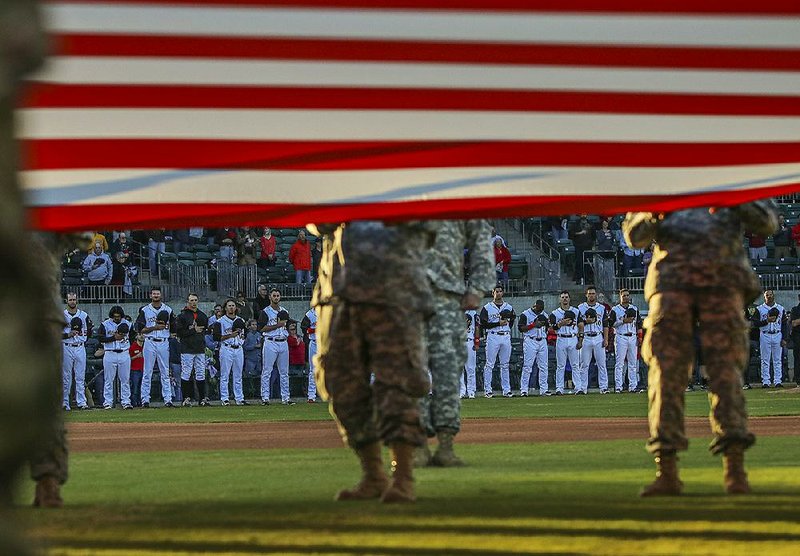 The Arkansas Travelers stand during the national anthem as members of the Arkansas Guard hold the American flag before the season opener against Corpus Christi on Thursday night at Dickey-Stephens Park in North Little Rock.