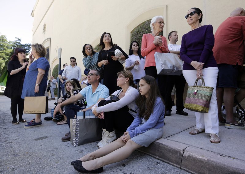 Shoppers Roman Lugo, seated, left, Siuris Rodriguez, center, and Chelsea Lugo, right, sit on the pavement after being evacuated from the Shops at Merrick Park after a shooting, Saturday, April 8, 2017, in Coral Gables, Fla. 